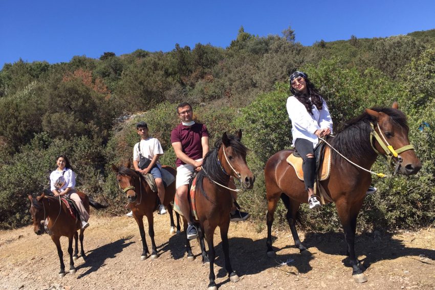 Güneşli bir günde orman yolunda Bodrum at safari turu deneyimi yaşayan ve at biniciliği yapan mutlu aile.