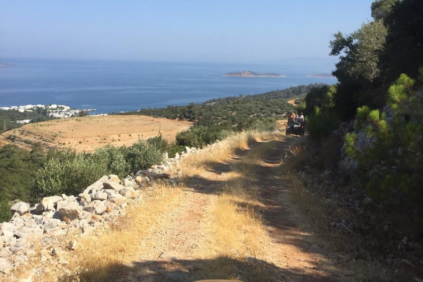 Bodrum Jeep Safari rotasında, arkasında eşsiz Ege Denizi ve adalar manzarasıyla dağlık toprak yoldan aşağı doğru ilerleyen üstü açık off-road araçları.