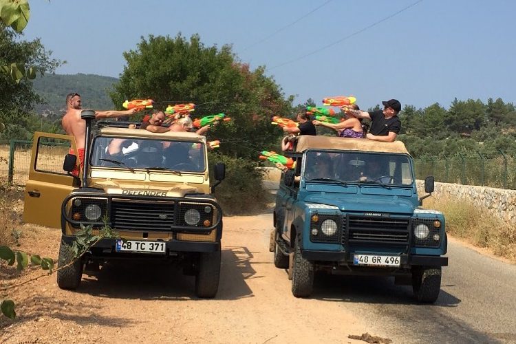 Bodrum Jeep Safari turunda yan yana duran iki üstü açık arazi aracındaki tatilcilerin renkli su tabancalarıyla yaptıkları eğlenceli su savaşı.
