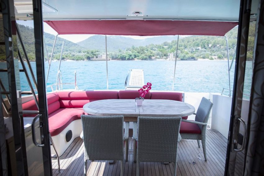 bodrum-torba-motoryat-kiralama (4) Bodrum Torba motoryat kiralama hizmeti sunan lüks teknenin aydınlık ve ferah ana salonu; modern bordo oturma grubu, şık yemek masası ve deniz manzaralı geniş pencereler.