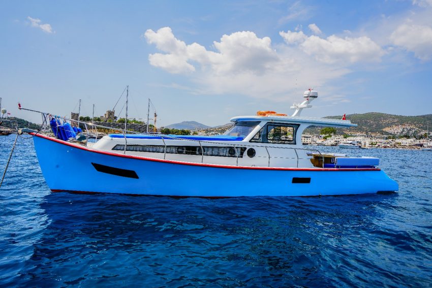 muge (2) Bodrum özel tekne kiralama hizmeti sunan göz alıcı mavi gövdesiyle Müge teknesinin, arka planda tarihi Bodrum Kalesi manzarasıyla Ege sularındaki şık dış görünümü.